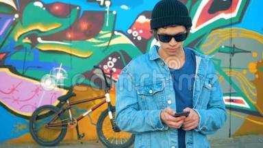 街上的墙上满是涂鸦，旁边还有一个男孩子带着智能手机